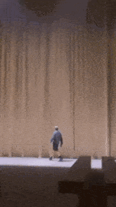 a man is walking on a stage with a curtain behind him .