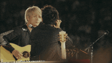 a man playing a guitar and another man singing into a microphone with the letter a on their shirt