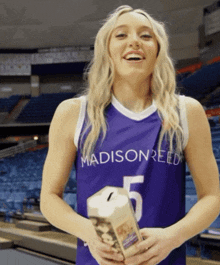 a woman wearing a purple madison reed jersey holds a piggy bank