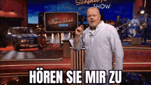 a man with a beard is standing in front of a sign that says „ hören sie mir zu ” .