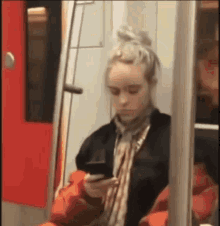 a woman is sitting on a train and looking at her phone .