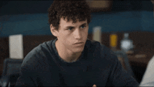 a young man with curly hair is sitting at a table talking to another man