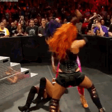 two women are wrestling in a ring in front of a crowd . one of the women has red hair .