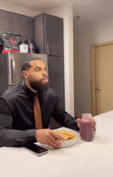 a man in a black shirt and tie is sitting at a table eating a bowl of food and drinking a smoothie .