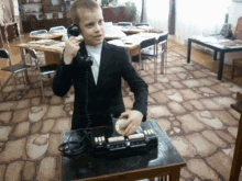 a boy in a suit is talking on an old fashioned telephone