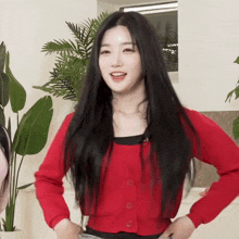 a woman in a red sweater is standing in front of a plant