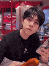 a young man sitting at a table holding a phone and a fried chicken