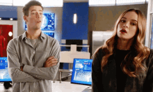 a man and a woman are standing next to each other with their arms crossed and a computer monitor in the background