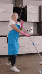a woman in a blue apron and pink gloves mopping the floor