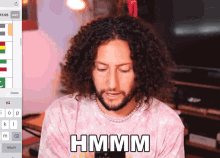 a man with curly hair and a beard is wearing a pink shirt that says hmm