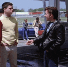 a man in a black leather jacket is talking to another man in a yellow sweater