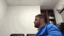 a man with a beard is sitting on a couch in a living room with his mouth open .