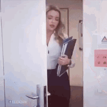 a woman is standing in a doorway holding a folder with a facebook logo on the bottom right