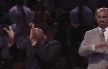 a man in a suit and tie is clapping his hands in a crowd .