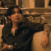 a man with a tattoo on his arm sits on a couch holding a can of soda
