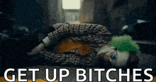 the joker is laying on the ground with the words `` get up bitches '' written on the bottom .