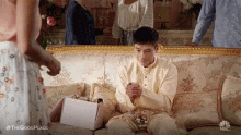 a man is sitting on a couch with a box of perfume in his hand .