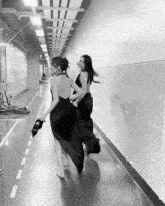 a black and white photo of two women walking down a hallway with the number 15 on the wall behind them