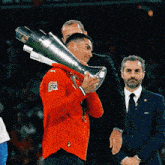 a man in a red puma shirt is holding a large trophy