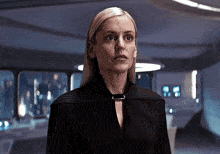 a woman in a black jacket is standing in a room looking at the camera .