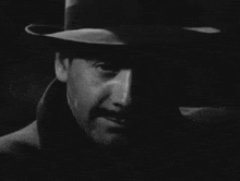 a man in a fedora looks at the camera in a black and white photo