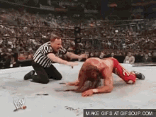a referee is kneeling down next to a wrestler in a wrestling ring