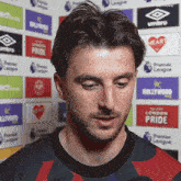 a man with a beard is talking into a microphone in front of a wall with logos for umbro and hollywood .
