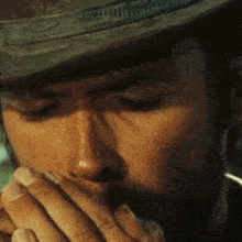 a close up of a man wearing a cowboy hat covering his mouth with his hands .