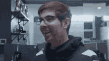 a man wearing glasses and a black hoodie smiles for the camera