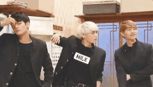 three young men are standing next to each other in a room and one of them is wearing a milk shirt .