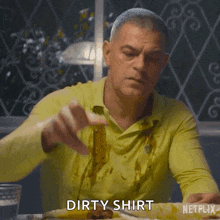 a man is sitting at a table with a dirty shirt on and a plate of food .