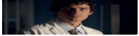 a man in a white coat and tie is standing in the dark .