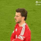 a man wearing a red shirt with white stripes on the sleeves is standing on a soccer field sponsored by tnt spor