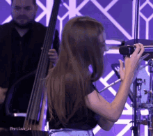 a woman is singing into a microphone while a man plays a double bass in the background