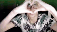 a man wearing glasses and a floral shirt is making a heart shape with his hands .