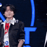 a man in a black jacket is standing in front of a blue letter t