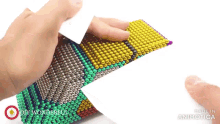 a person is holding a piece of paper over a pile of colorful beads made in animatica
