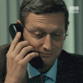 a man wearing glasses is talking on a telephone with hbo max written on the bottom