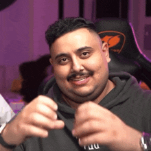 a man with a mustache is making a funny face while wearing a black hoodie and a watch .
