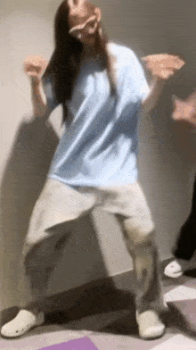 a woman in a blue shirt and gray pants is dancing on a floor .