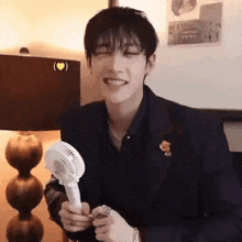 a young man in a suit is holding a small fan in his hand and smiling .