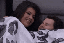 a man and a woman are laying under a blanket and the woman is smiling .