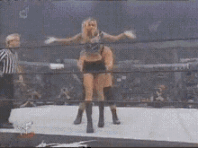 two wrestlers are fighting in a ring with a referee in the background .