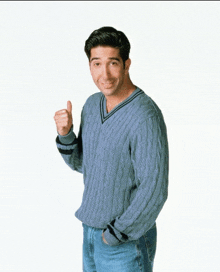 a man wearing a blue sweater and jeans gives a thumbs up