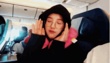 a woman wearing a hoodie and glasses is sitting on a plane .