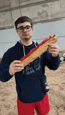 a man wearing a blue hoodie that says nb energy is holding a large sandwich