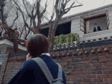 a man in a suit and tie looks out of a window while a woman talks on a cell phone