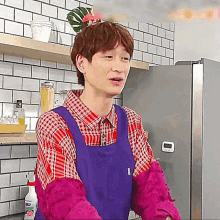 a man wearing a purple apron and a plaid shirt stands in front of a refrigerator