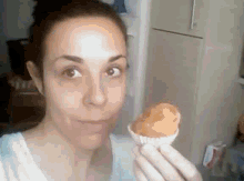 a woman is holding a cupcake in her hand in front of a refrigerator .