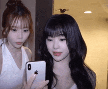 two women are looking at a cell phone together .